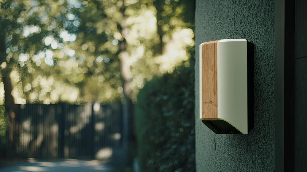 Andersen Quartz EV charger in light cream and wood finish installed on a textured green exterior wall, blending with a leafy residential driveway.